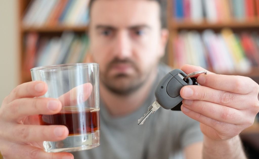 image of a man holding up an alcoholic drink and a car key